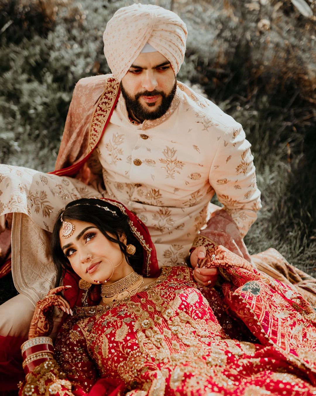 Young Indian Bride groom posing for photograph during their wedding. The  couple is wearing traditional indian wedding dress which is designer red  lehenga for bride and sherwani for groom foto de Stock |
